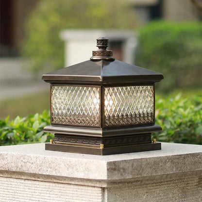Outdoor pillar light with bronze metal frame and patterned glass shade installed on stone pillar in garden setting ideal for landscape lighting.