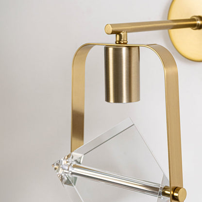 Detailed closeup of clear crystal cube glass shade and brushed brass gold metal frame hardware on modern wall sconce fixture.