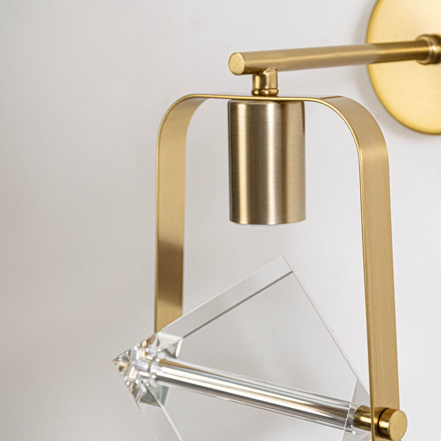 Detailed closeup of clear crystal cube glass shade and brushed brass gold metal frame hardware on modern wall sconce fixture.