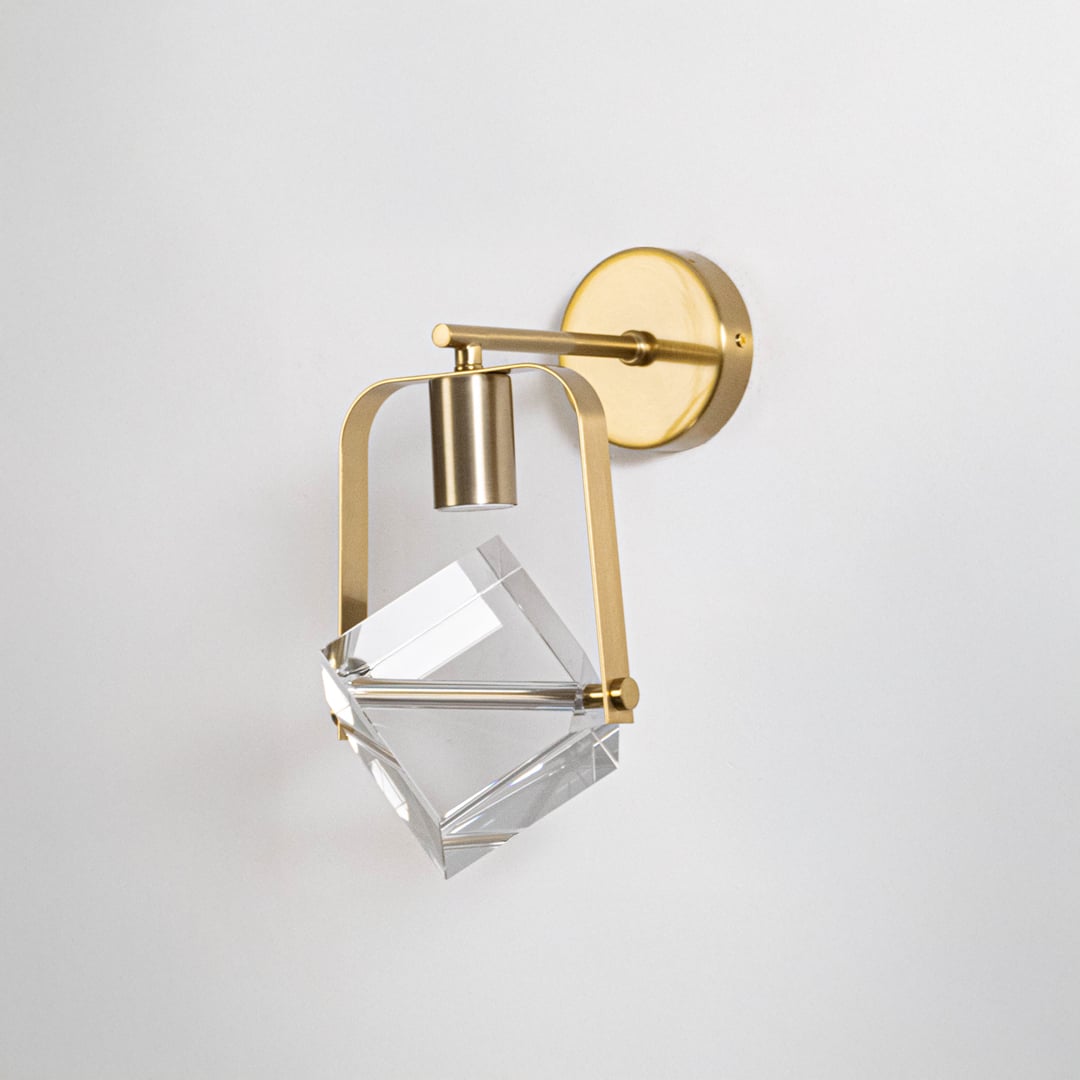 Elegant brass gold metal wall light fixture with clear crystal cube glass shade turned off on minimalist white background.
