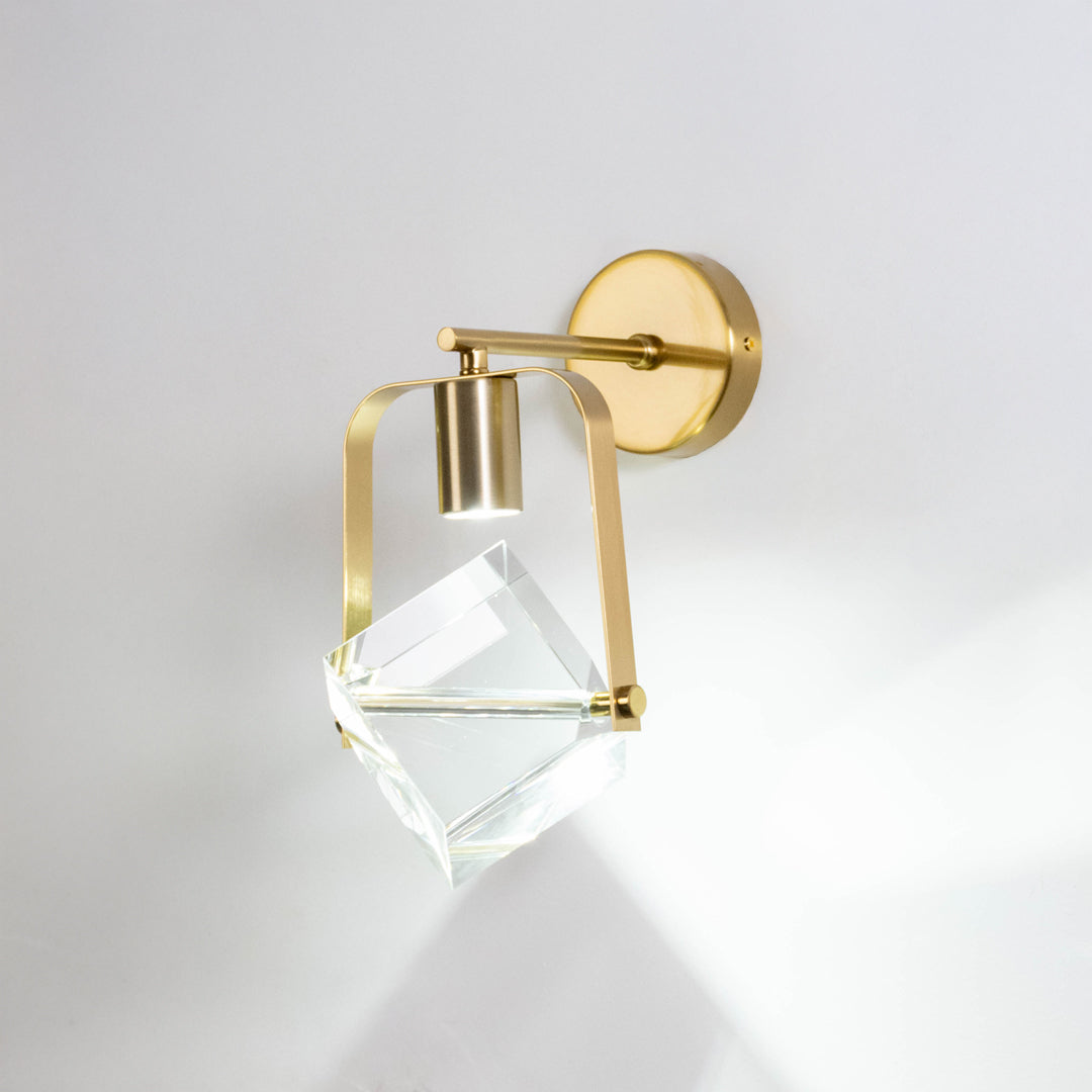 Gold metal crystal wall light on white background with geometric glass shade for luxury modern wall decor.