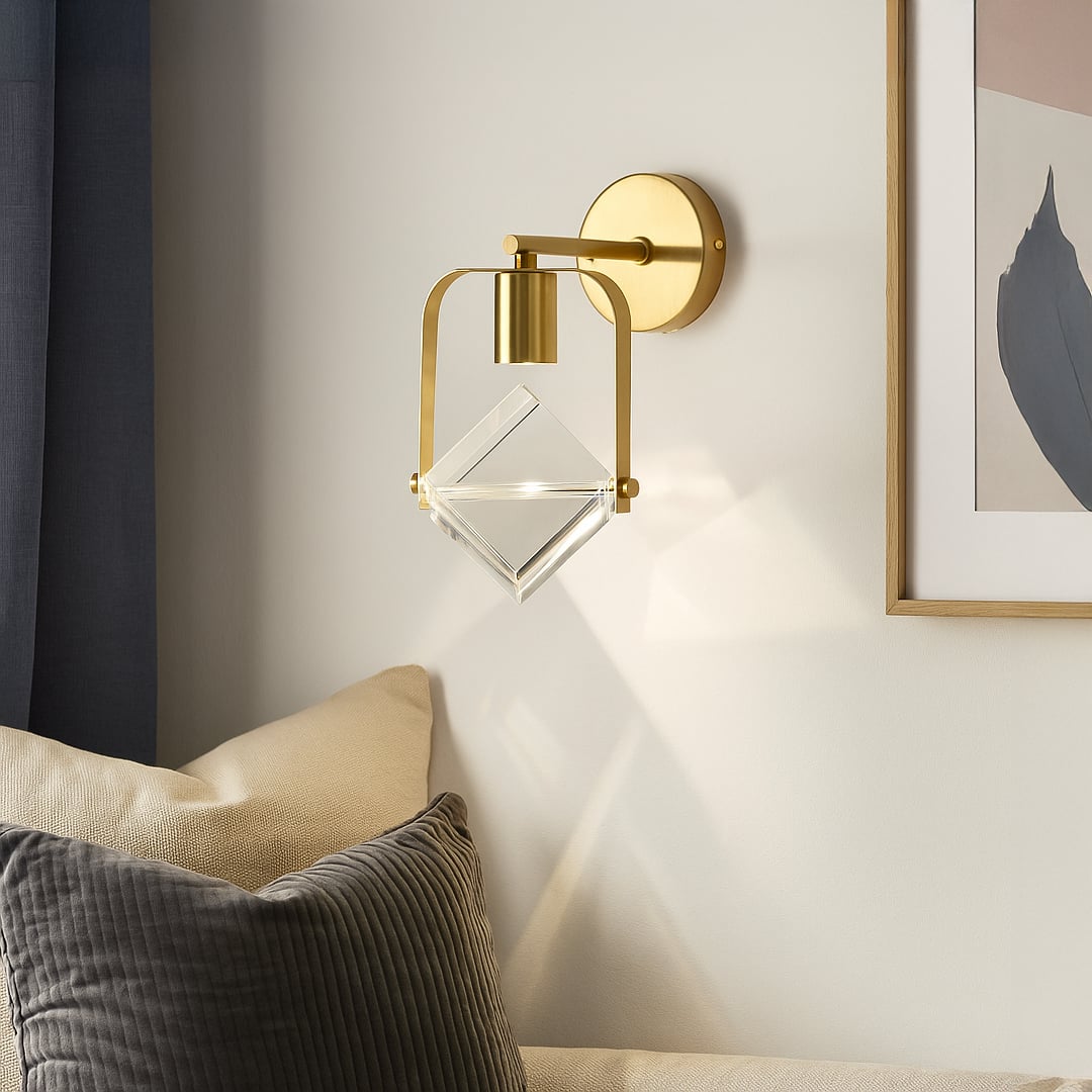 Modern brass gold wall sconce with clear crystal cube shade mounted on interior wall creating luxurious contemporary lighting.