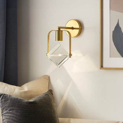 Modern brass gold wall sconce with clear crystal cube shade mounted on interior wall creating luxurious contemporary lighting.
