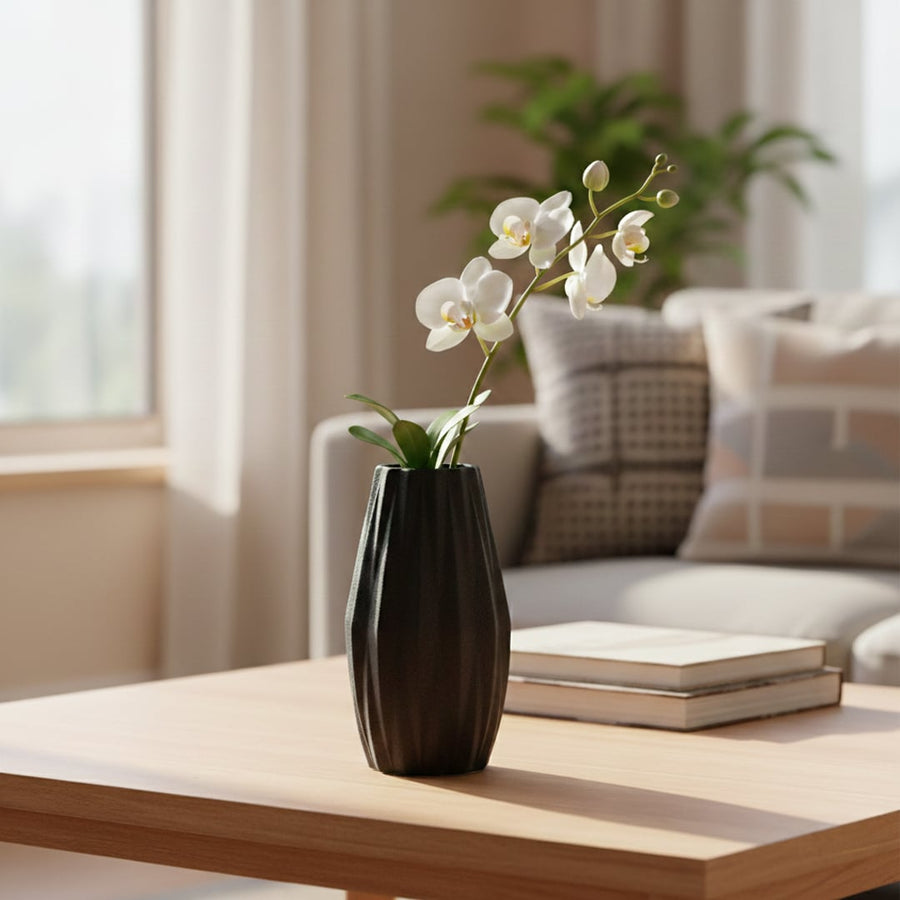 Black textured ceramic decorative vase styled with orchid stem on wooden coffee table in bright modern living room setting.