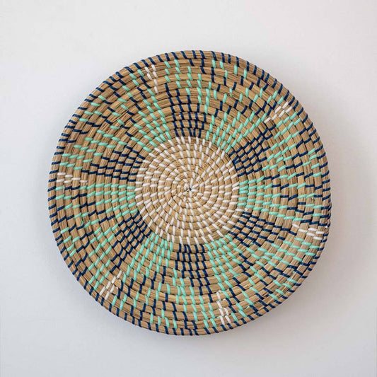 Handwoven seagrass round wall basket decor in natural beige green and brown with spiral woven pattern on white background.