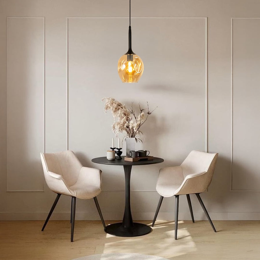 Amber glass pendant light hanging above dining table with beige chairs for modern home decor.
