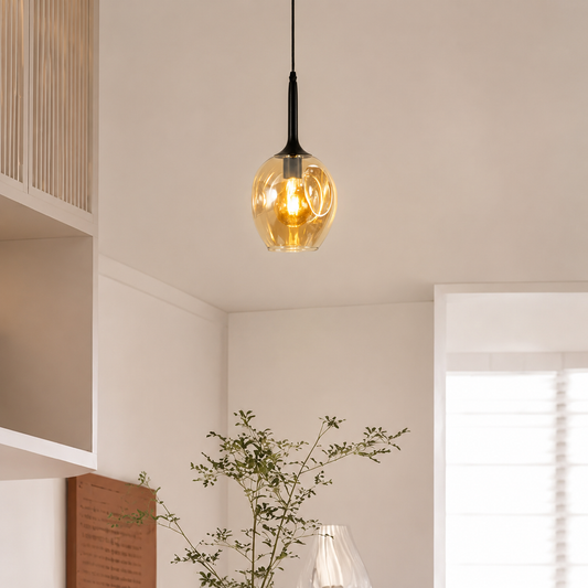 A modern pendant light with a warm glowing amber glass globe shade and a black metal neck, hanging from a ceiling in a minimalist room.