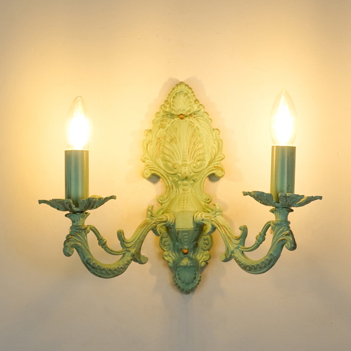 White background image of illuminated distressed green cast aluminium wall sconce for elegant rustic living room styling.