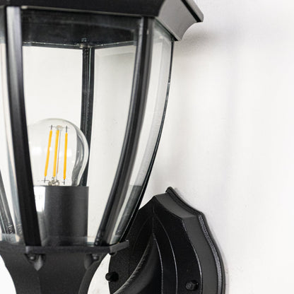 Black metal outdoor wall lantern closeup highlighting curved frame clear glass panels and exposed filament bulb for classic exterior lighting.