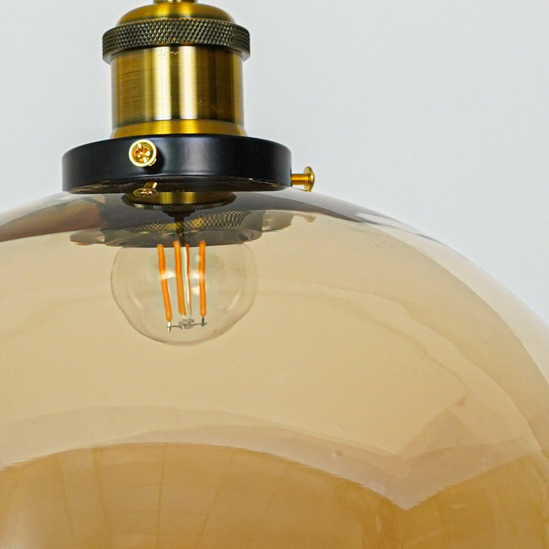 Amber glass dome pendant light with brass metal fixture showcasing glossy finish and contemporary lighting style.