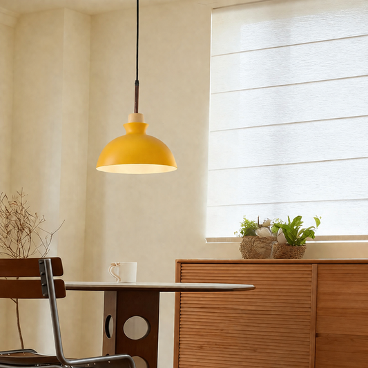 A modern yellow dome pendant light hanging over a dining table in a warm, minimalist room with a window, wooden cabinet, and small potted plants.