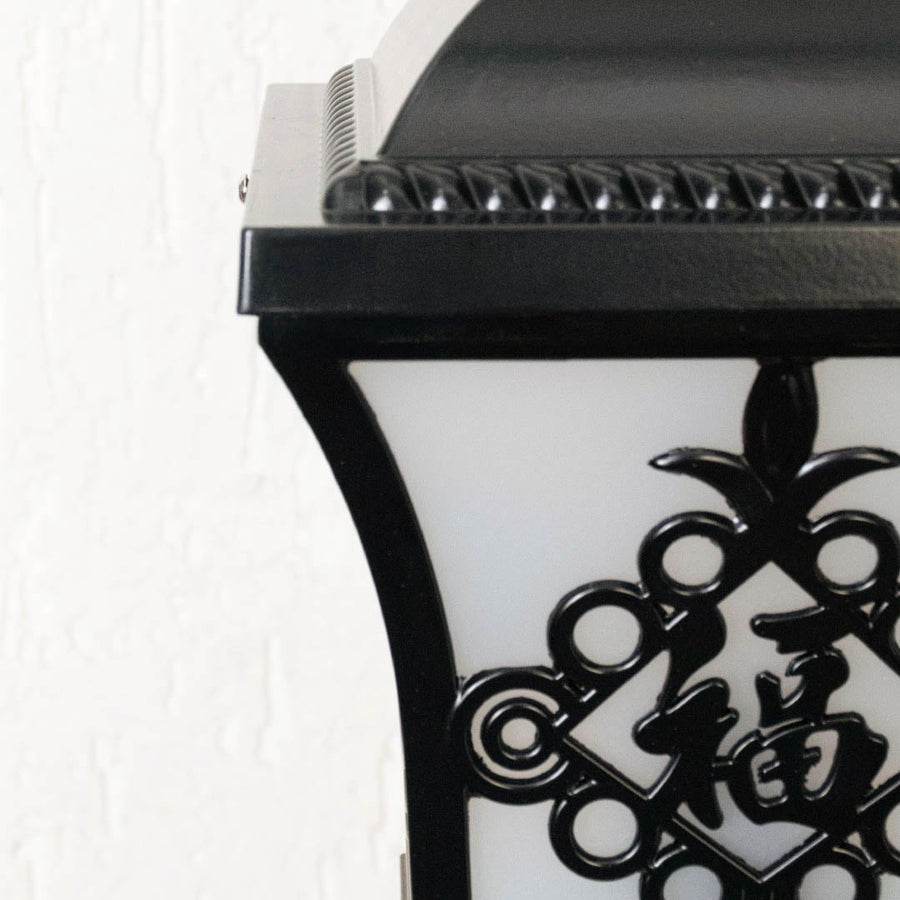 Black outdoor post light seeded glass Closeup Light On showing the textured glass and black metal base detailing on a column.