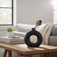 Black ceramic ring vase styled on a wooden coffee table adding sculptural elegance to modern living room decor.