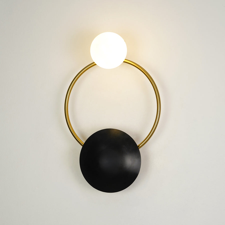 Contemporary gold brass hoop wall sconce featuring an illuminated frosted glass globe bulb on a white backdrop.