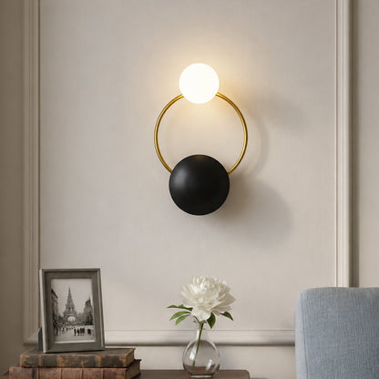 Modern gold brass hoop wall sconce with black plate accent and glowing glass orb bulb mounted in a luxury living room.