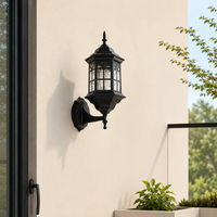 Traditional black iron upward hexagonal grid glass wall lantern sconce on white exterior facade for home porch lighting.