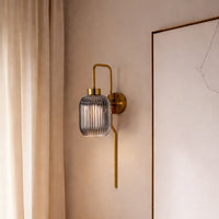 Modern gold wall light with ribbed glass shade styled beside wall creating warm ambient glow for elegant interior decor.
