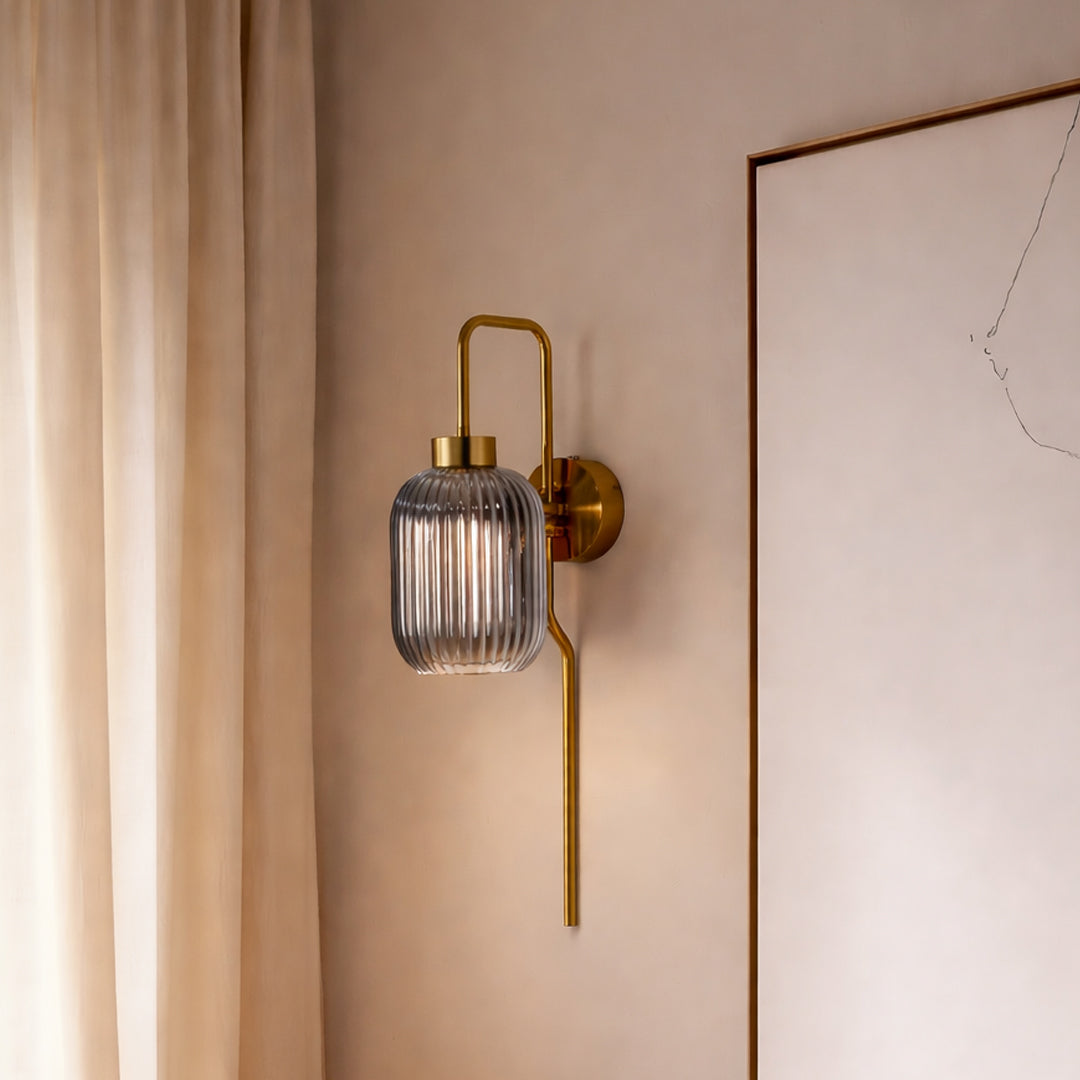 Modern gold wall light with ribbed glass shade styled beside wall creating warm ambient glow for elegant interior decor.