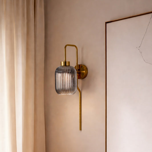Modern gold wall light with ribbed glass shade styled beside wall creating warm ambient glow for elegant interior decor.
