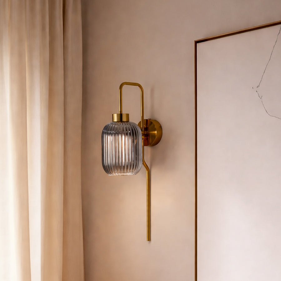 Modern gold wall light with ribbed glass shade styled beside wall creating warm ambient glow for elegant interior decor.