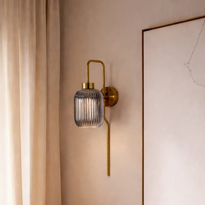 Modern gold wall light with ribbed glass shade styled beside wall creating warm ambient glow for elegant interior decor.