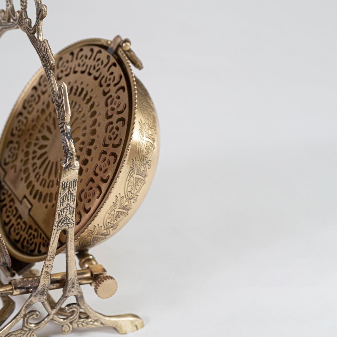 A closeup view of the brass swing bowl highlights the engraved floral patterns the curved lid handle and the detailed carved frame showcasing fine craftsmanship.