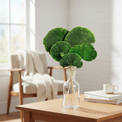 Vibrant green preserved fan palm leaves in a clear glass vase on a wooden side table next to a living room armchair setup.
