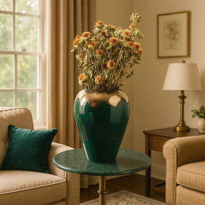 Green ceramic vase with gold accent filled with dried orange flowers placed on a round side table creating a warm elegant lifestyle decor accent for living rooms.