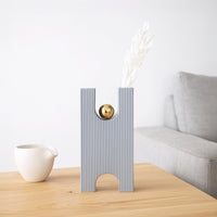 Modern decorative ceramic vase with ribbed texture and gold accent styled on wooden table in a calm contemporary living room setting.