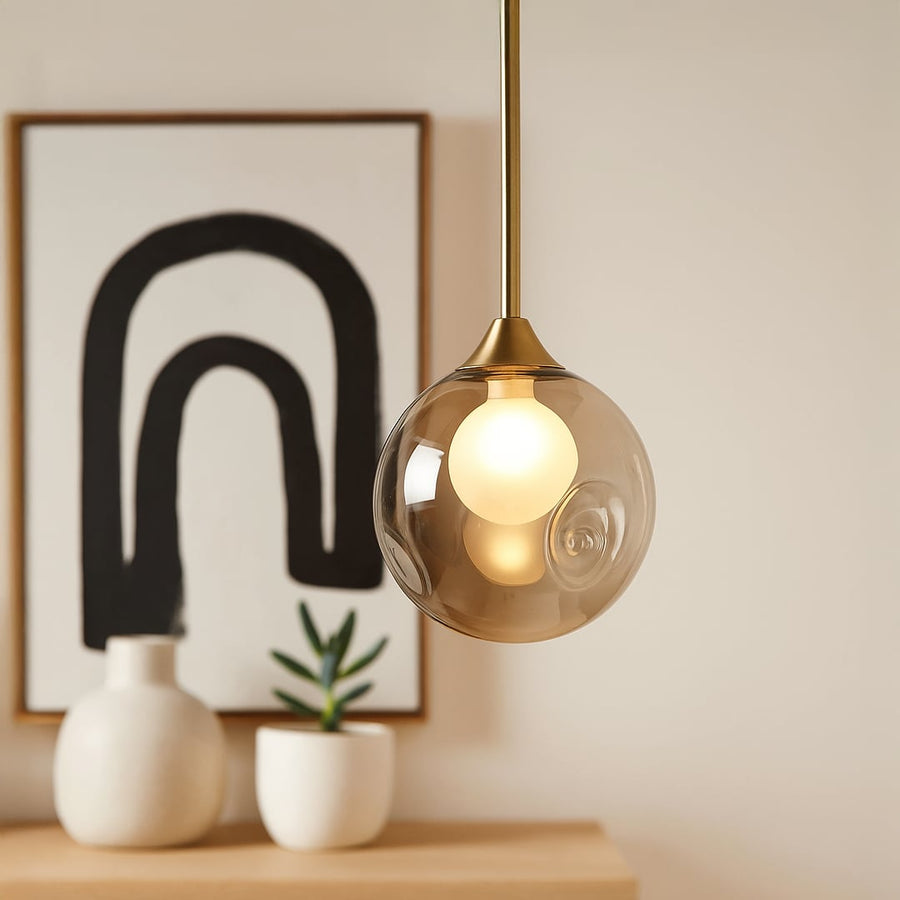 Modern smoked grey glass globe pendant lamp with brass rod displayed off on white background for home and interiors.