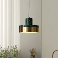 A modern pendant light with a dark green marble top and a brushed gold metal shade, suspended by a black cord against a neutral indoor background.