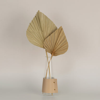 Two natural dried palm spear leaves arranged in a clear glass vase on a light background.