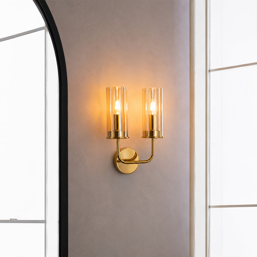 Elegant gold brass double candle wall sconce illuminated beautifully on an entryway wall next to a large mirror.