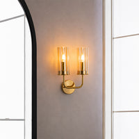 Elegant gold brass double candle wall sconce illuminated beautifully on an entryway wall next to a large mirror.