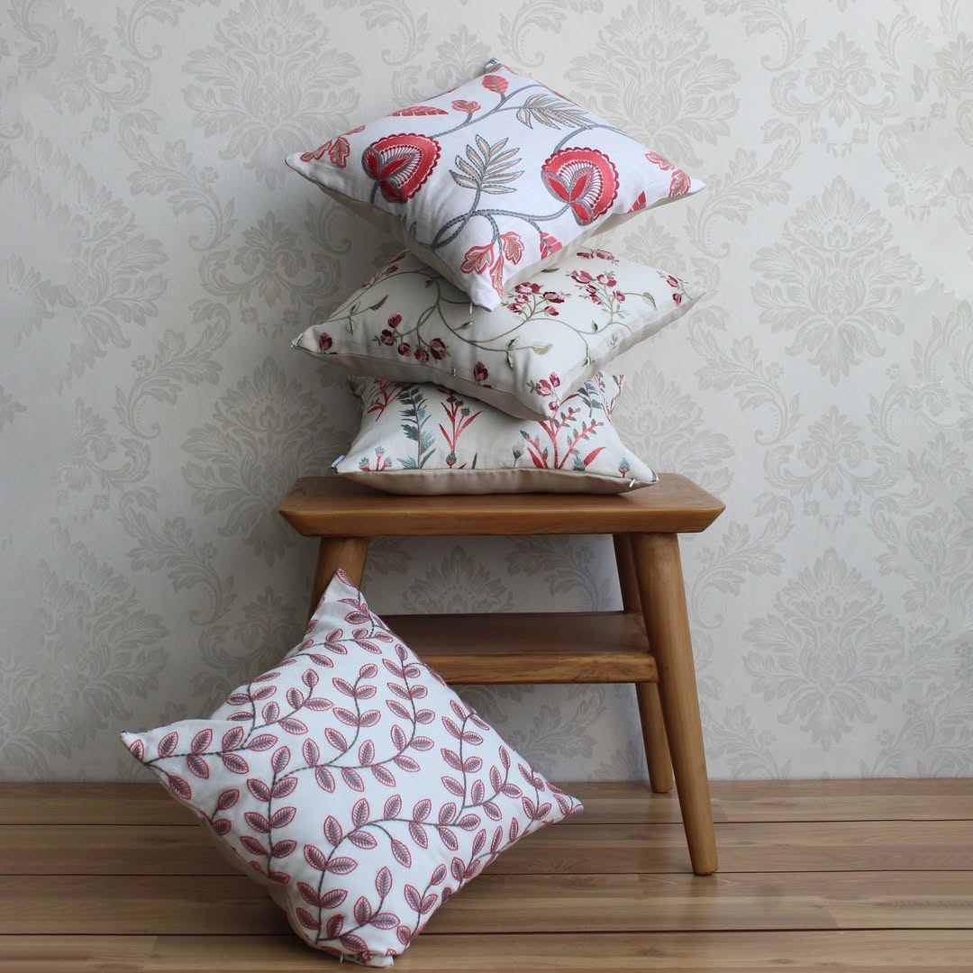 Soft cotton cushion cover with pink floral design stacked with matching covers offering a warm nature inspired look that elevates home décor with a smooth skin friendly texture.