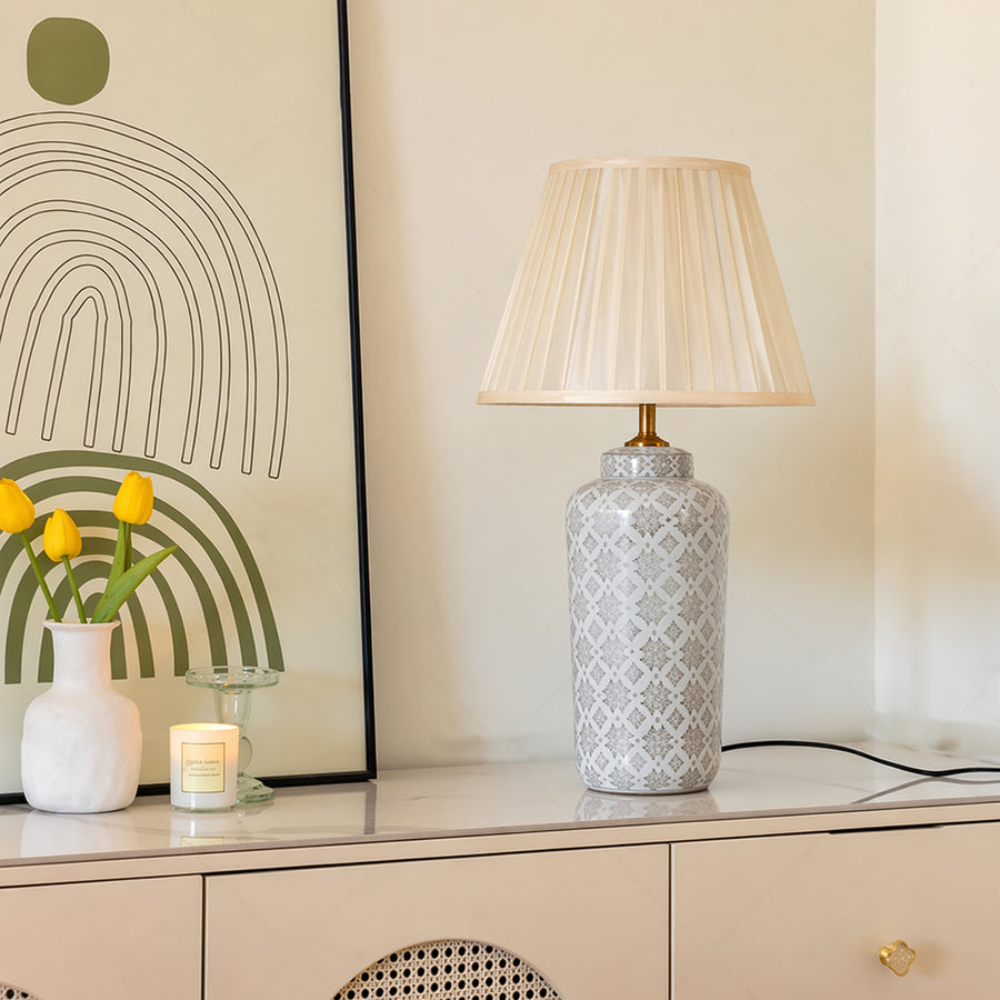 Grey patterned ceramic table lamp with pleated fabric shade placed on a sideboard creating elegant ambient lighting indoors.