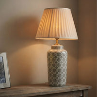 Elegant grey patterned ceramic table lamp featuring a pleated cream fabric shade styled on a rustic wooden console desk.