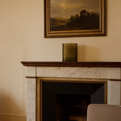 Decorative ribbed metal vase placed on classic fireplace mantel beneath framed artwork creating warm elegant living room decor accent.