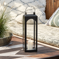 Modern black metal outdoor lantern with clear glass panels creating warm decorative lighting for patios and garden spaces.