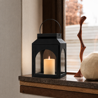 Modern black metal candle lantern with clear glass panels displayed on a wooden table creating cozy ambient lighting.