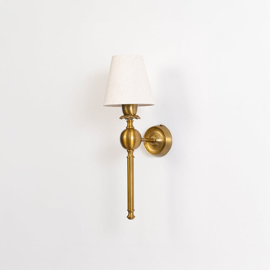 Classic brass gold torch wall lamp fixture with a tapered white fabric cone shade mounted on a plain white background.