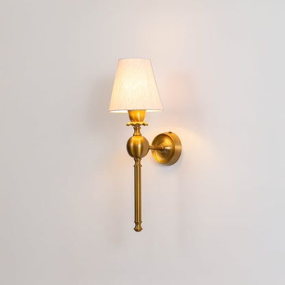 Elegant brushed gold metal traditional wall sconce light turned on to show a bright glow through a pleated fabric shade.