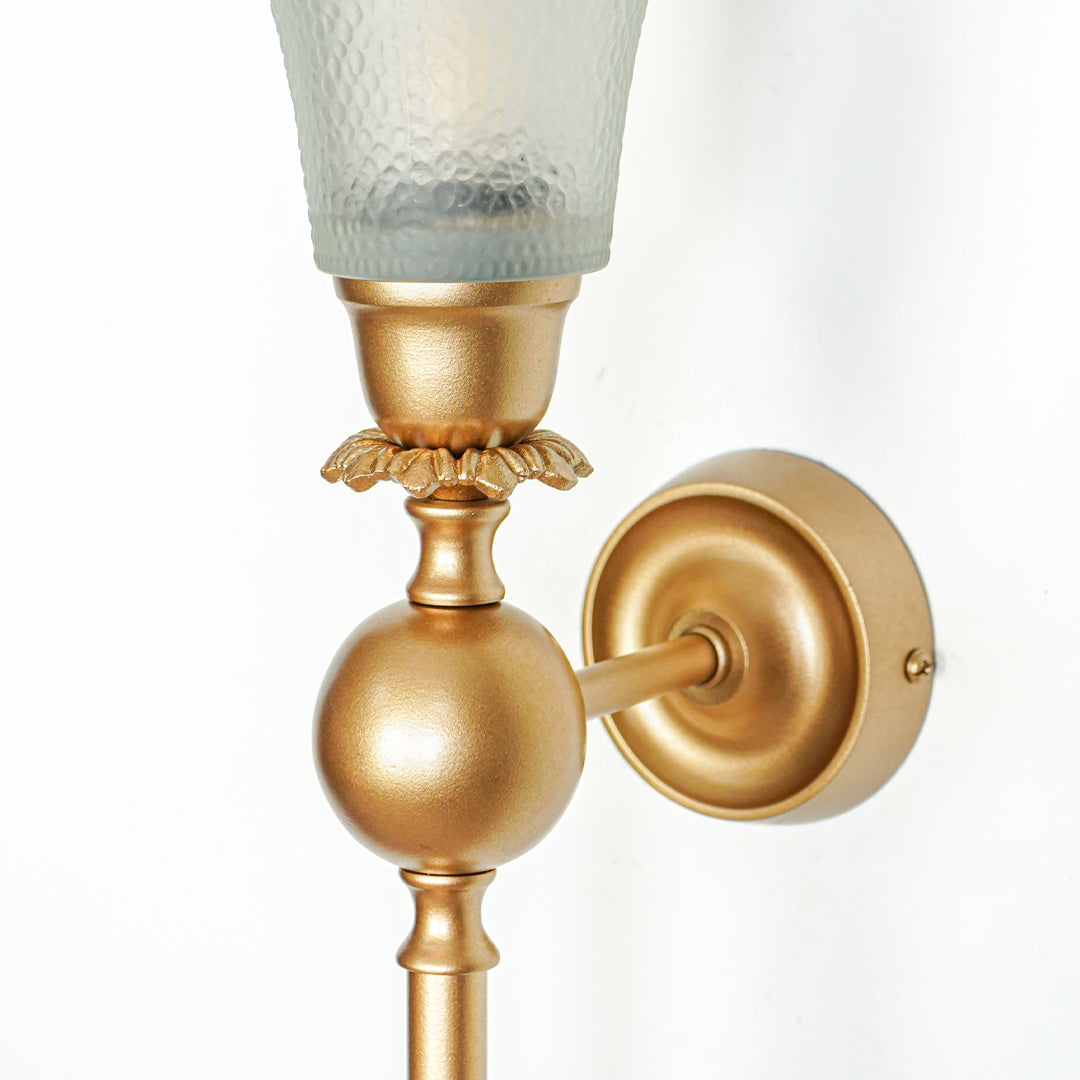 Closeup of gold metal wall light with textured glass shade and metal base on white background perfect for premium interior decor.