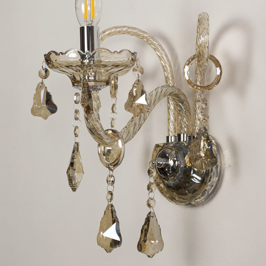 Closeup of champagne wall light showing twisted glass arms and crystal drops for refined elegant interior lighting.