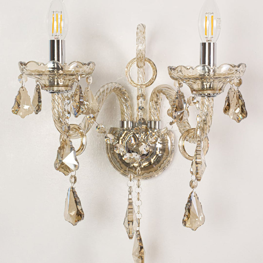 Closeup of champagne wall light showing twisted glass arms and crystal drops for refined elegant interior lighting.