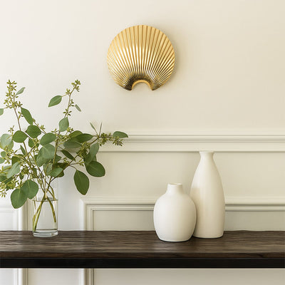 A gold shell shaped decor piece displayed in a soft lifestyle setting offering a modern elegant look that enhances any interior space beautifully.