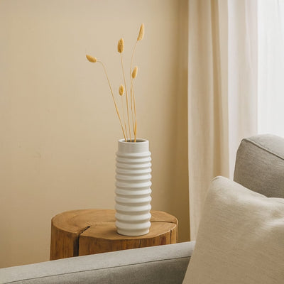 Decorative ceramic table vase in white finish placed on wooden side table beside sofa adding modern accent to living room decor.