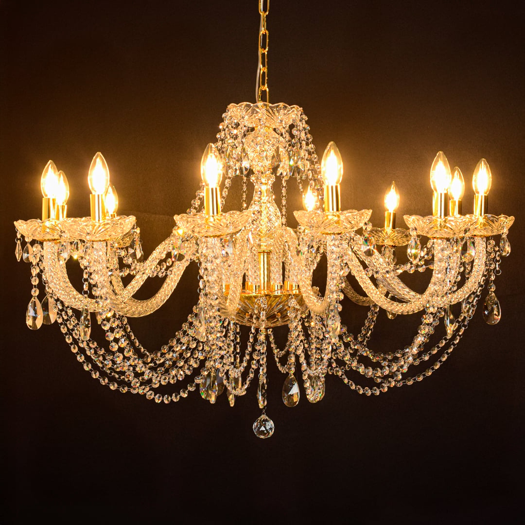 Large gold crystal chandelier glowing warmly on black background creating a dramatic luxury ceiling feature.