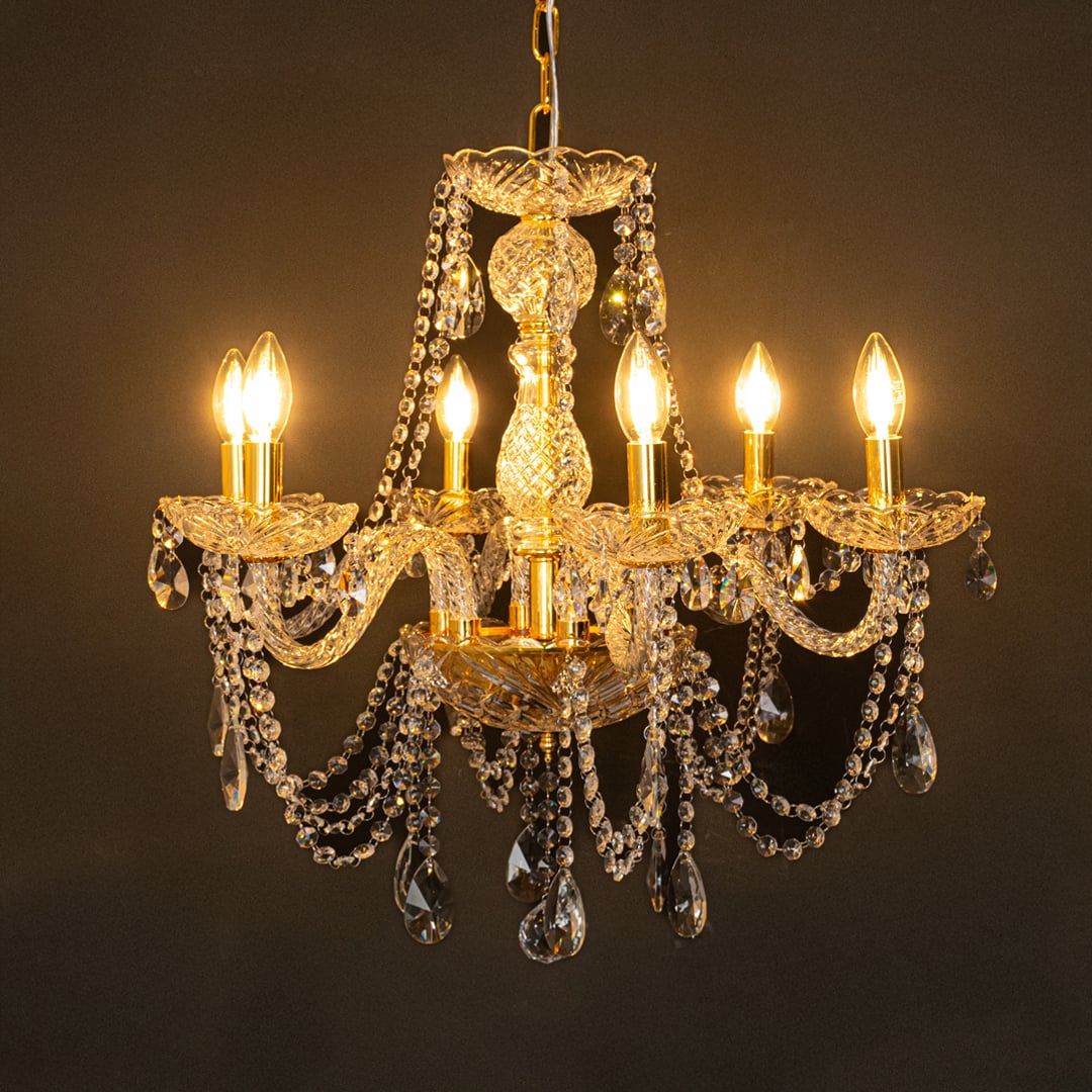 Gold metal crystal chandelier glowing warmly on black background creating a dramatic luxury ceiling feature.