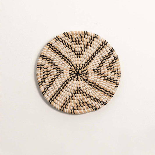 Round handcrafted black and natural seagrass wall basket with geometric chevron star X pattern on white background image.